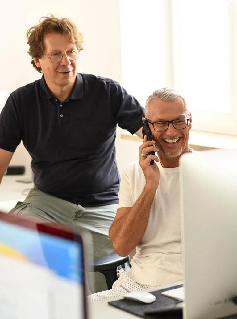 Zwei Mitarbeiter der Agentur Heldenstreich im kreativen Austausch im Büro, während einer telefoniert.