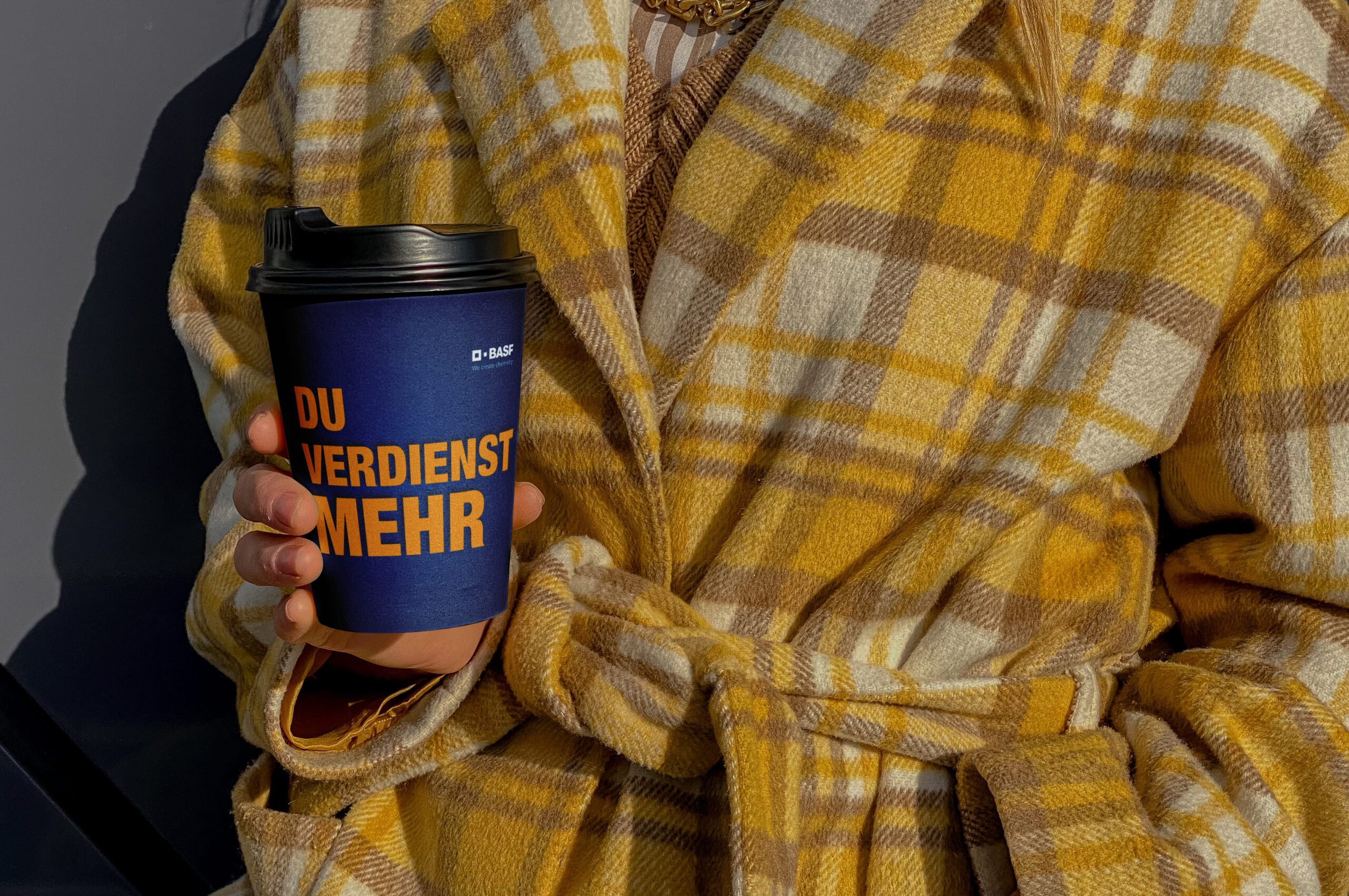 Hand hält einen gebrandeten Coffee-to-go-Becher mit dem Claim „Du verdienst mehr“ – Recruiting-Merchandising von BASF Coatings Würzburg im Corporate Design.