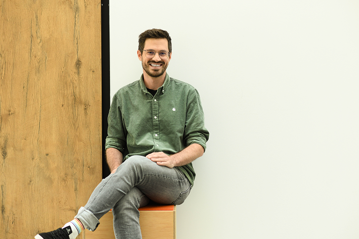 Mitarbeiter von Boehringer Ingelheim sitzt entspannt auf einem Holzpodest in moderner Büroumgebung.