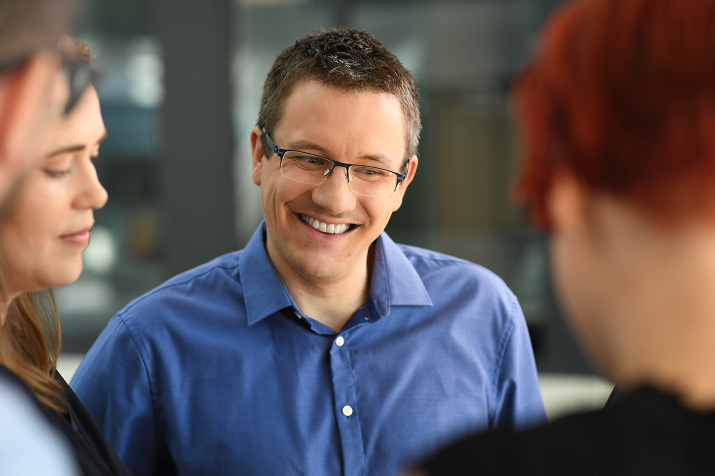 Lächelnder Mitarbeiter von Boehringer Ingelheim im Gespräch mit Kolleg*innen in moderner Büroumgebung.