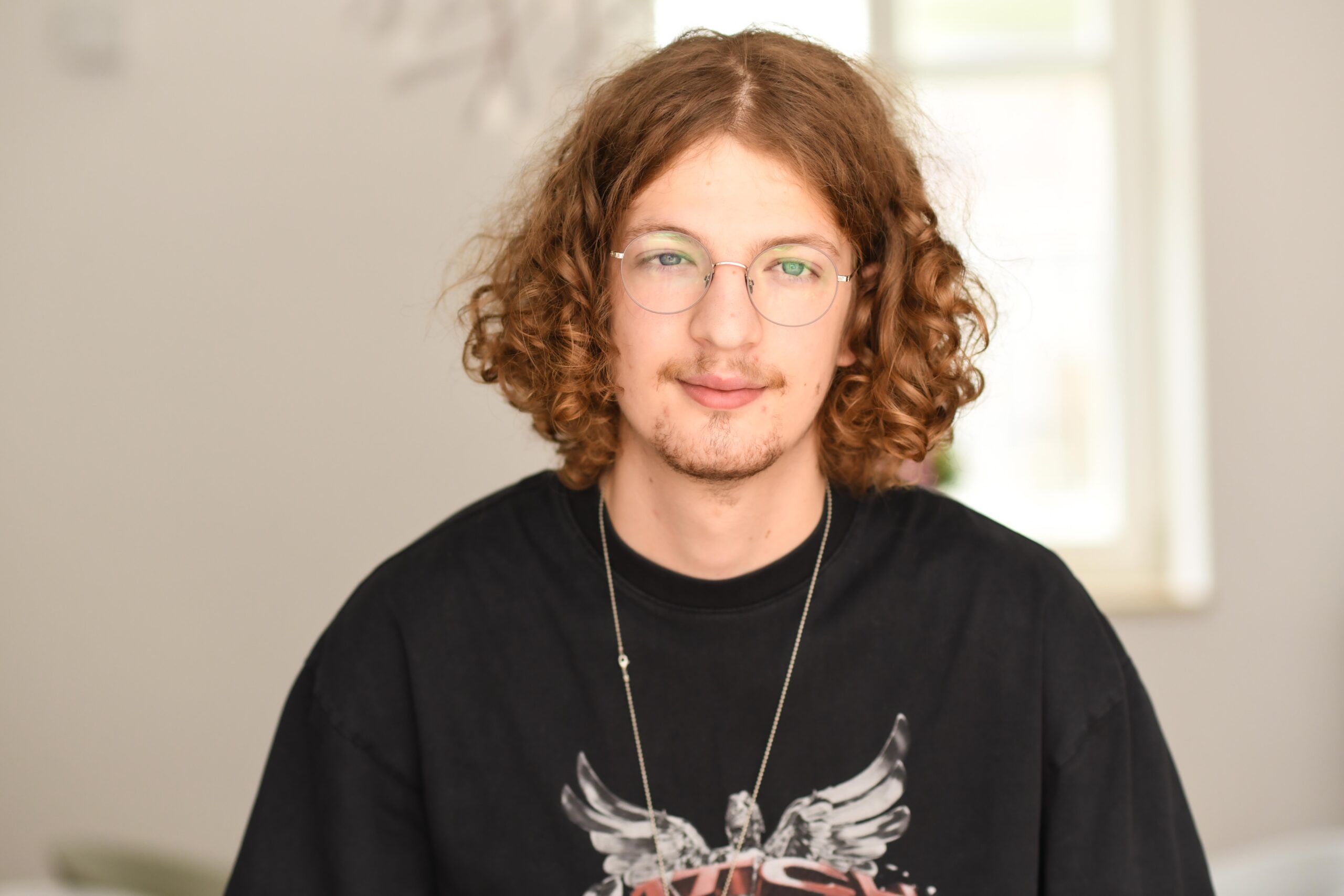 Junger Mitarbeiter mit lockigen Haaren und Brille blickt freundlich in die Kamera; Porträtfoto für die Agentur Heldenstreich.