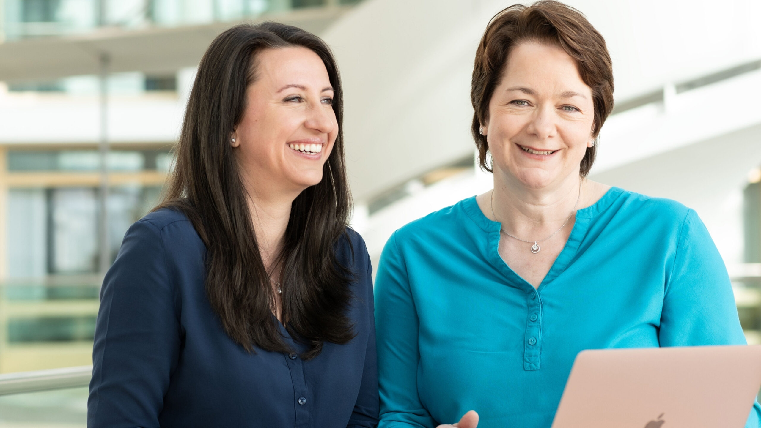 Zwei Mitarbeiterinnen von Boehringer Ingelheim im Gespräch, lächelnd vor modernem Bürohintergrund.