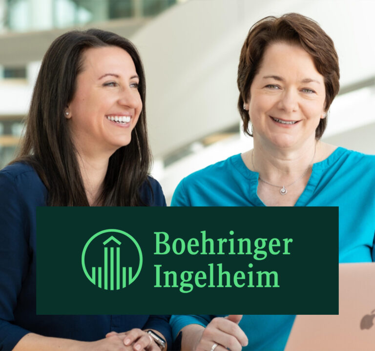 Zwei Mitarbeiterinnen von Boehringer Ingelheim sitzen gemeinsam lächelnd an einem Arbeitsplatz.