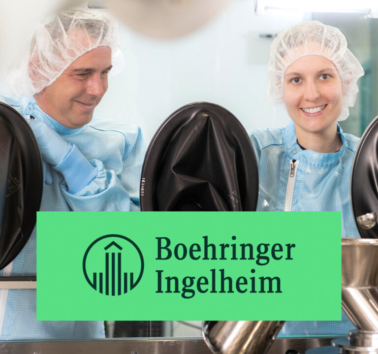 Mitarbeiterinnen und Mitarbeiter in steriler Produktionskleidung arbeiten an einem Reinraumarbeitsplatz bei Boehringer Ingelheim.