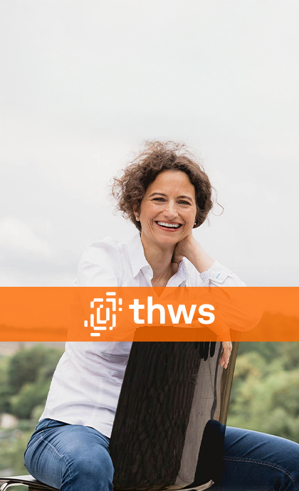 Professorin der THWS sitzt lächelnd im Außenbereich und blickt freundlich in die Kamera.
