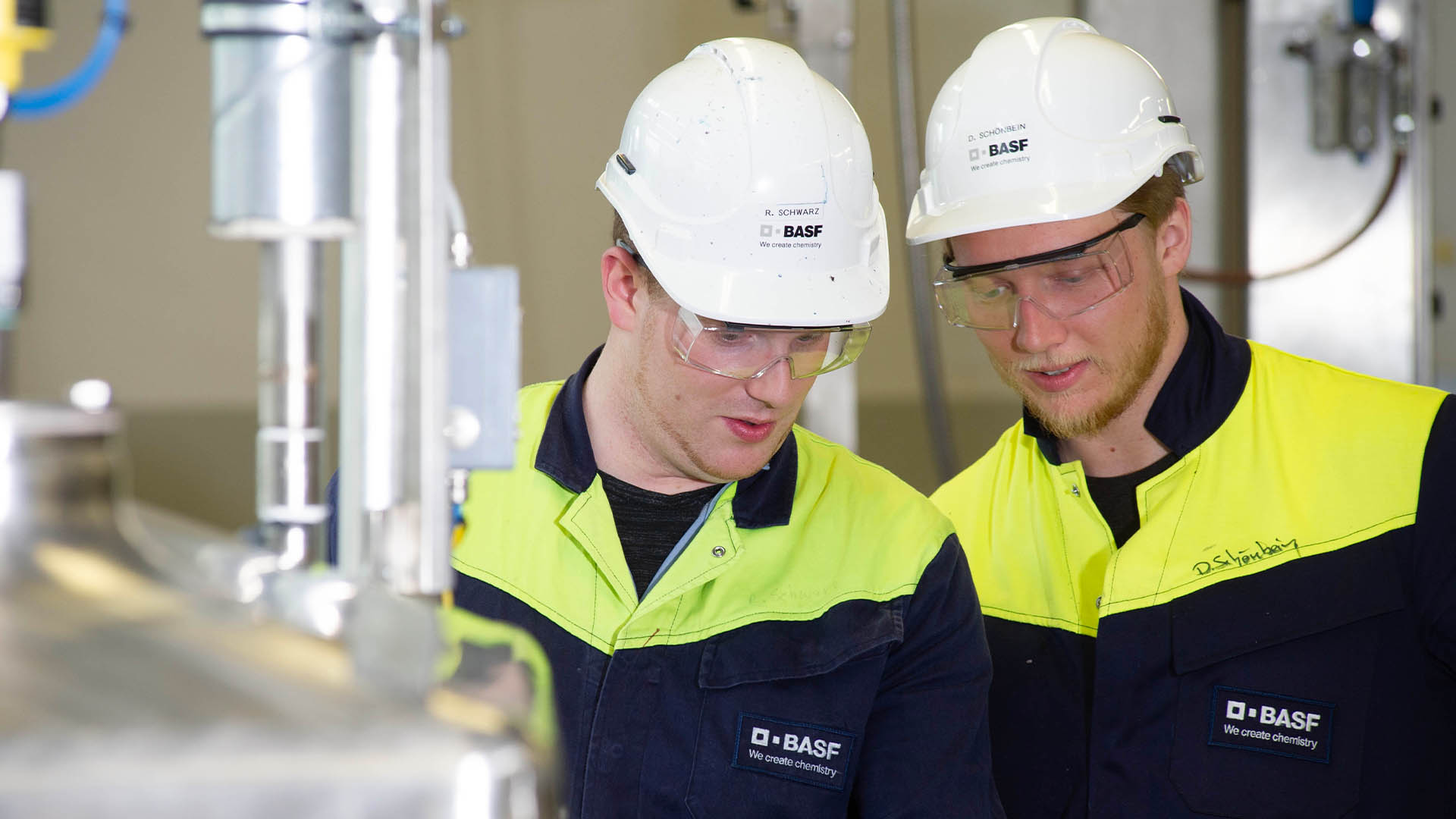 Zwei Mitarbeitende von BASF Coatings Würzburg mit Schutzhelm und Schutzbrille arbeiten gemeinsam an einer Anlage.