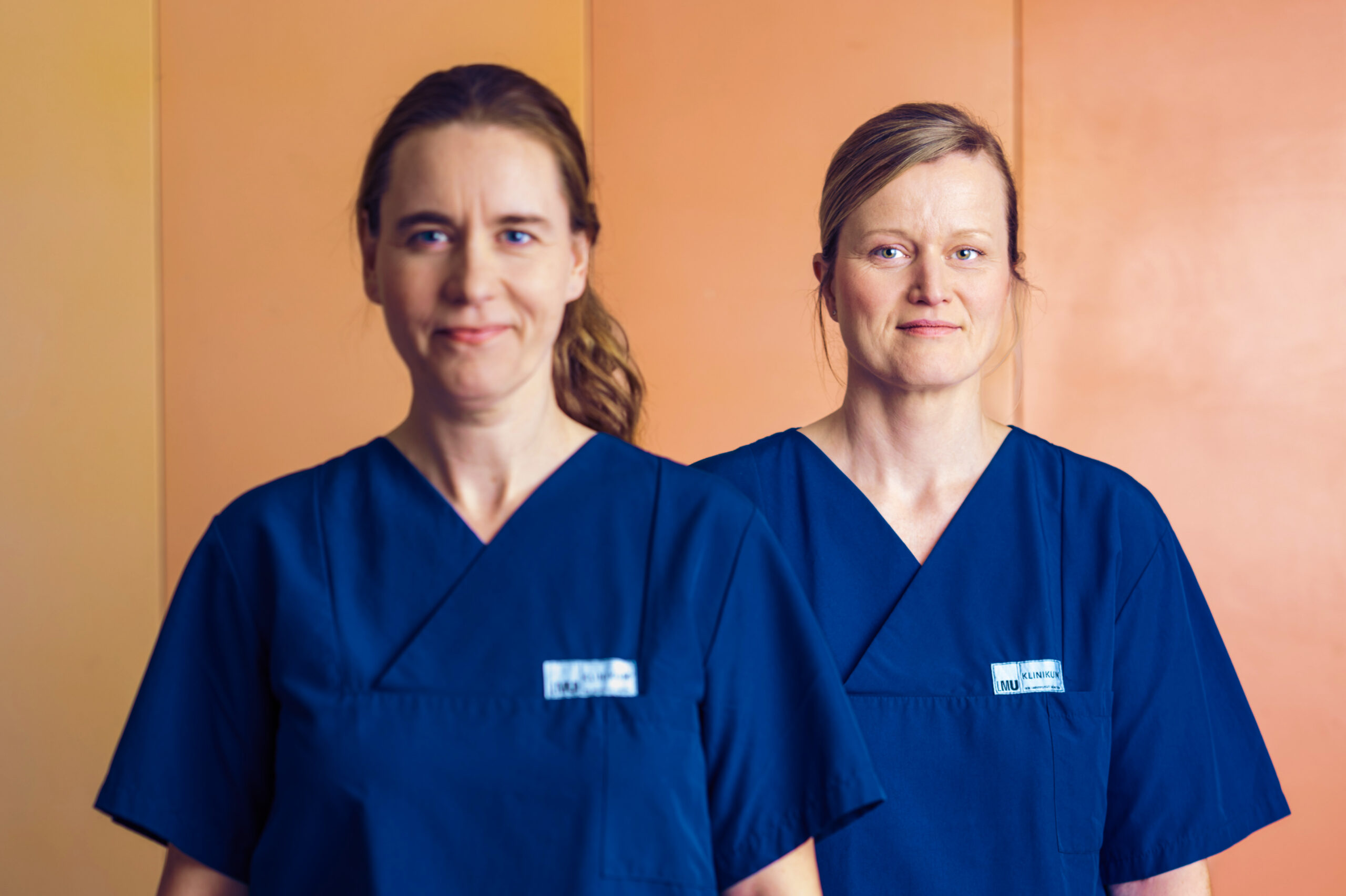 Zwei Pflegekräfte des LMU Klinikums im Portrait vor orangefarbenem Hintergrund.
