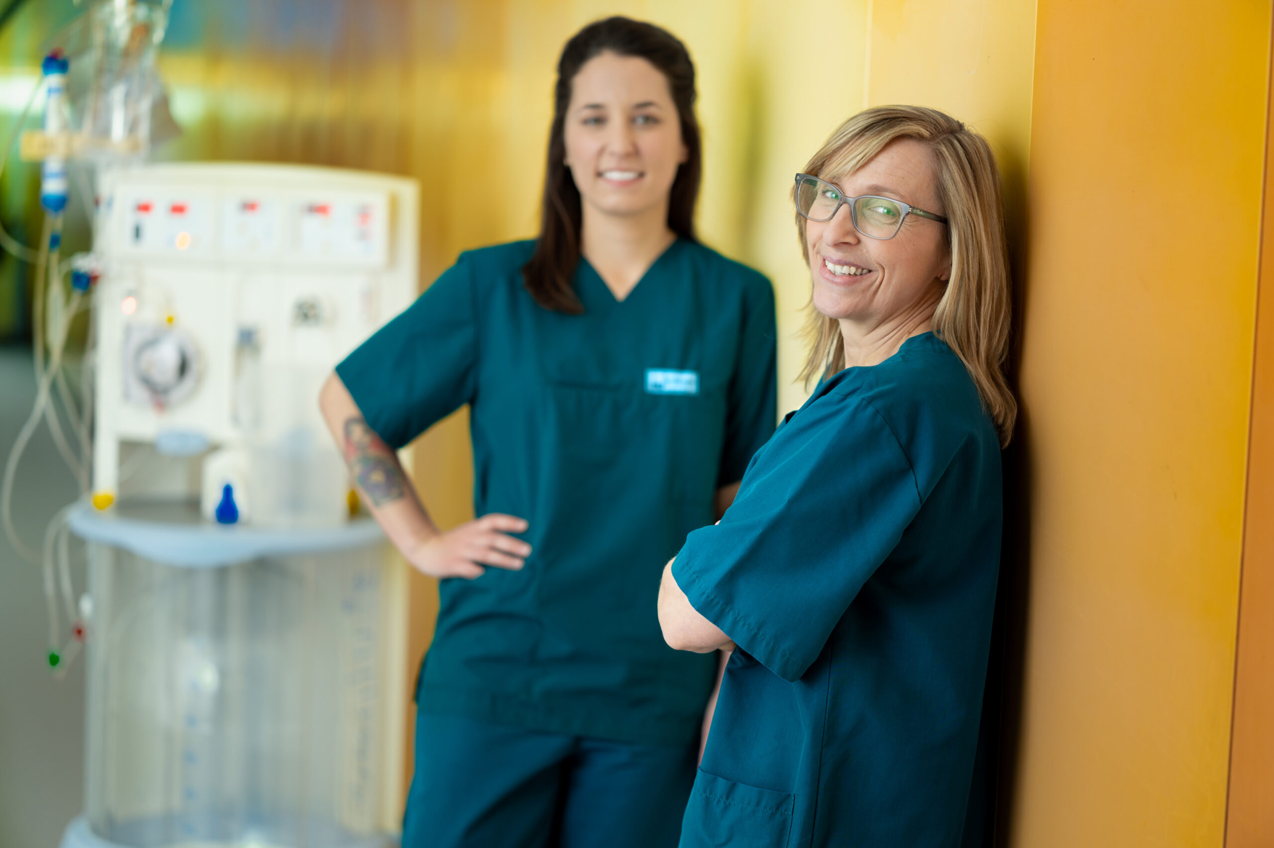 Zwei Mitarbeitende des LMU Klinikums in Pflegekleidung lächeln in die Kamera, moderne Krankenhausumgebung