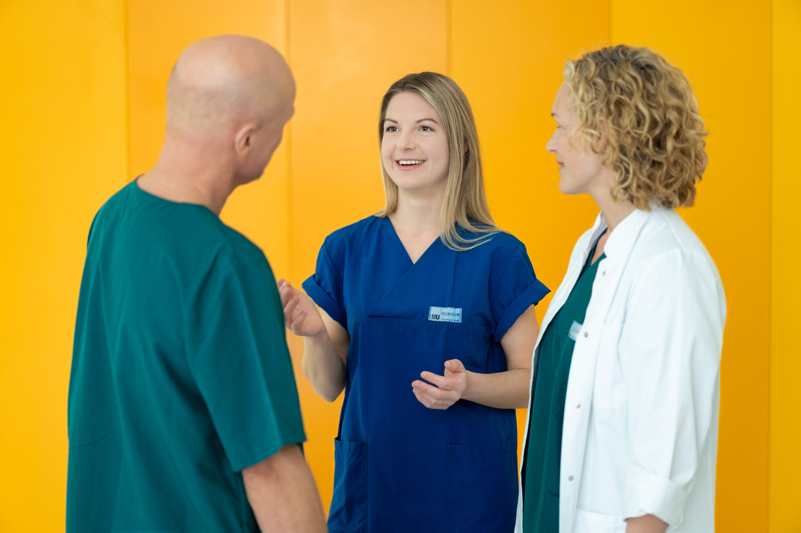 Pflegekräfte des LMU Klinikums im Gespräch vor einer gelben Wand