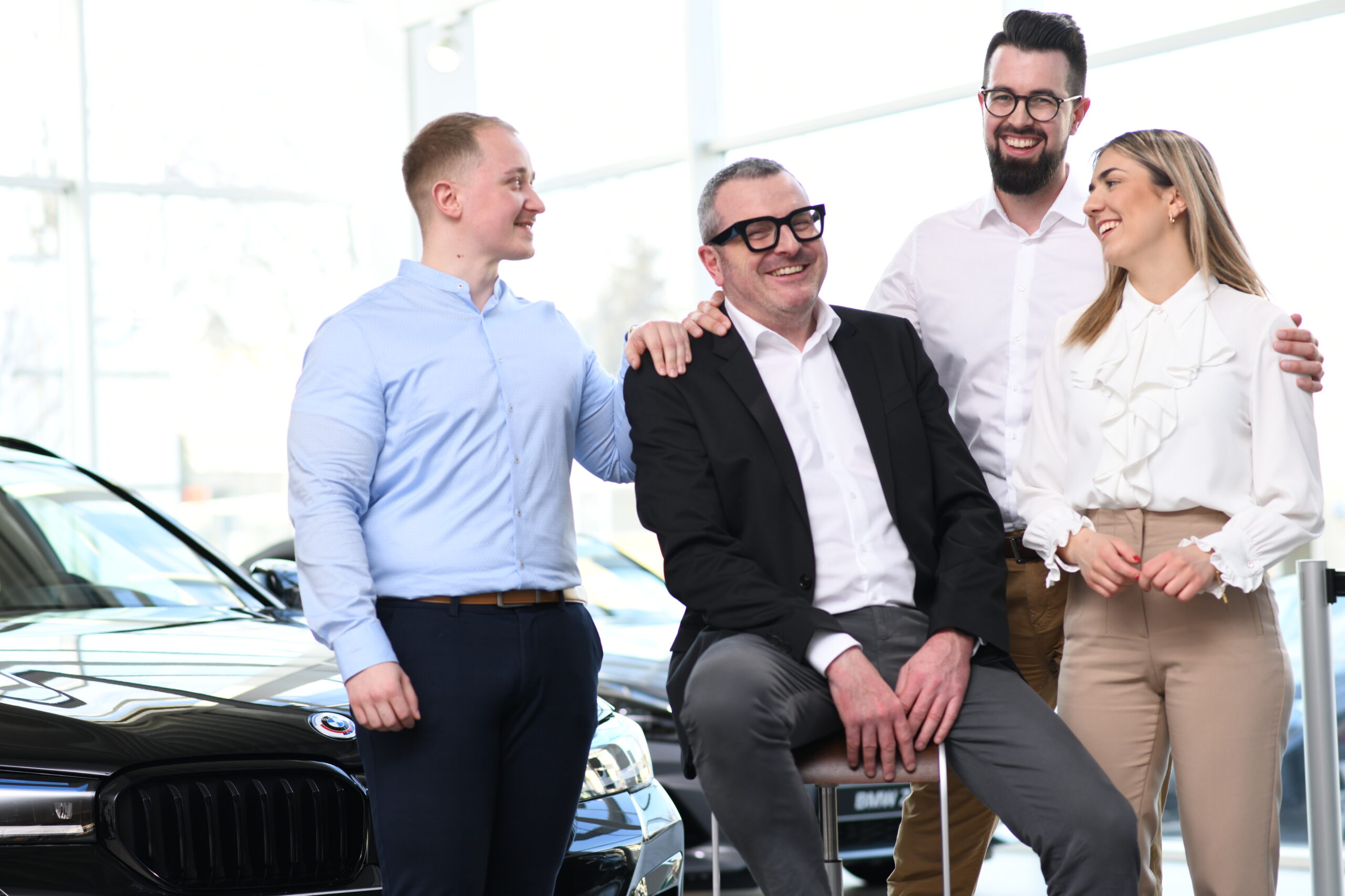 Vier Mitarbeitende von Widmann + Winterholler stehen lachend im Autohaus vor einem BMW und posieren für ein Employer-Branding-Foto.