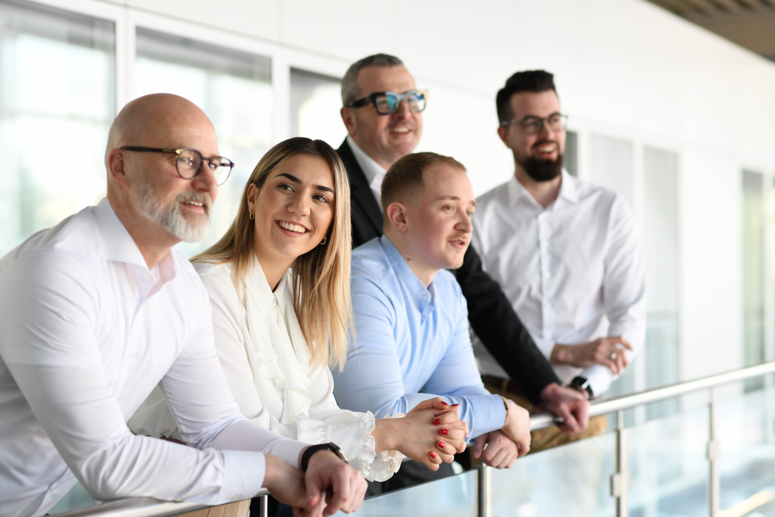 Gruppe von Mitarbeitenden bei Widmann Winterholler lehnt lächelnd am Geländer in einem modernen Autohaus.