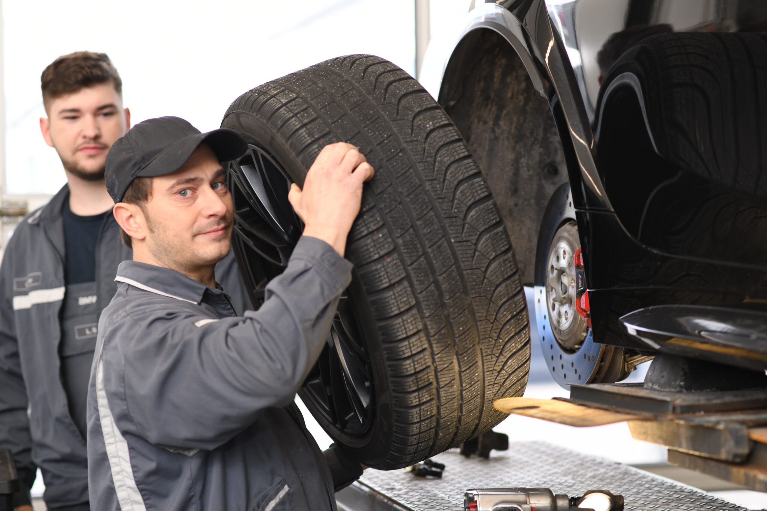 Mechaniker hebt ein Auto­rad während des Reifenwechsels in der Werkstatt bei Widmann + Winterholler