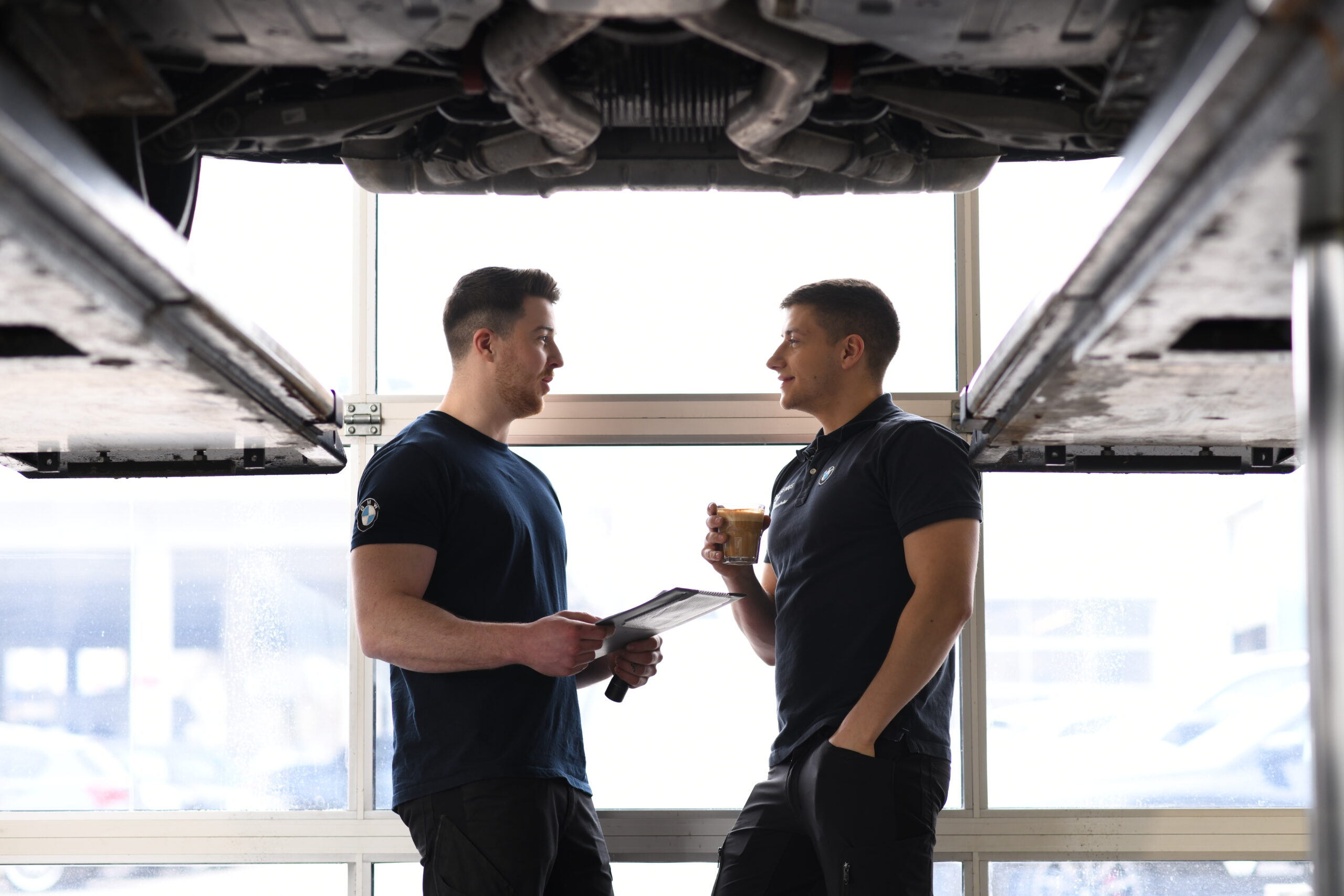 Mechaniker im BMW Autohaus unter einem angehobenen Fahrzeug im Gespräch