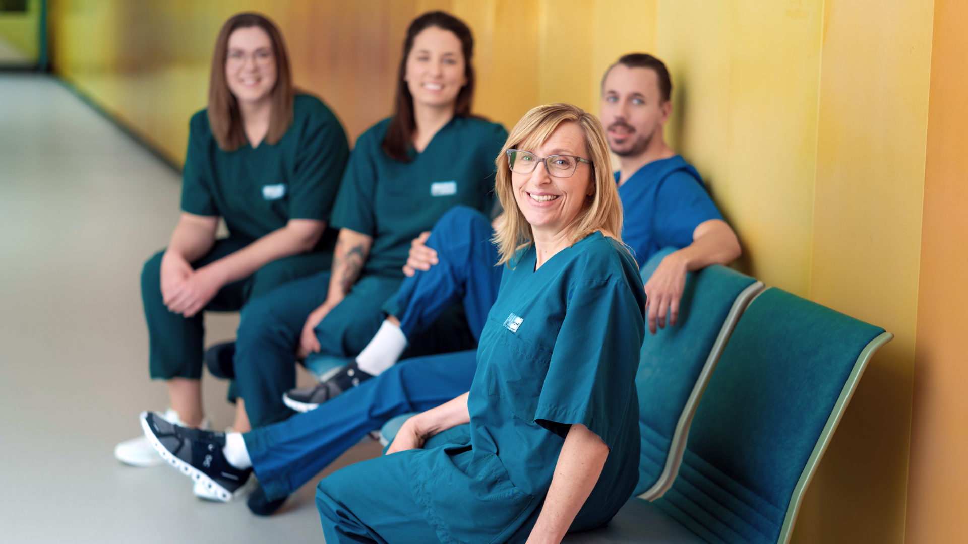 Pflegekräfte des LMU Klinikums sitzen gemeinsam auf einer Sitzbank und lächeln in die Kamera