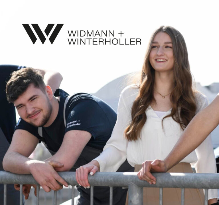 Junge Mitarbeitende von Widmann + Winterholler lehnen lächelnd am Geländer im Außenbereich.