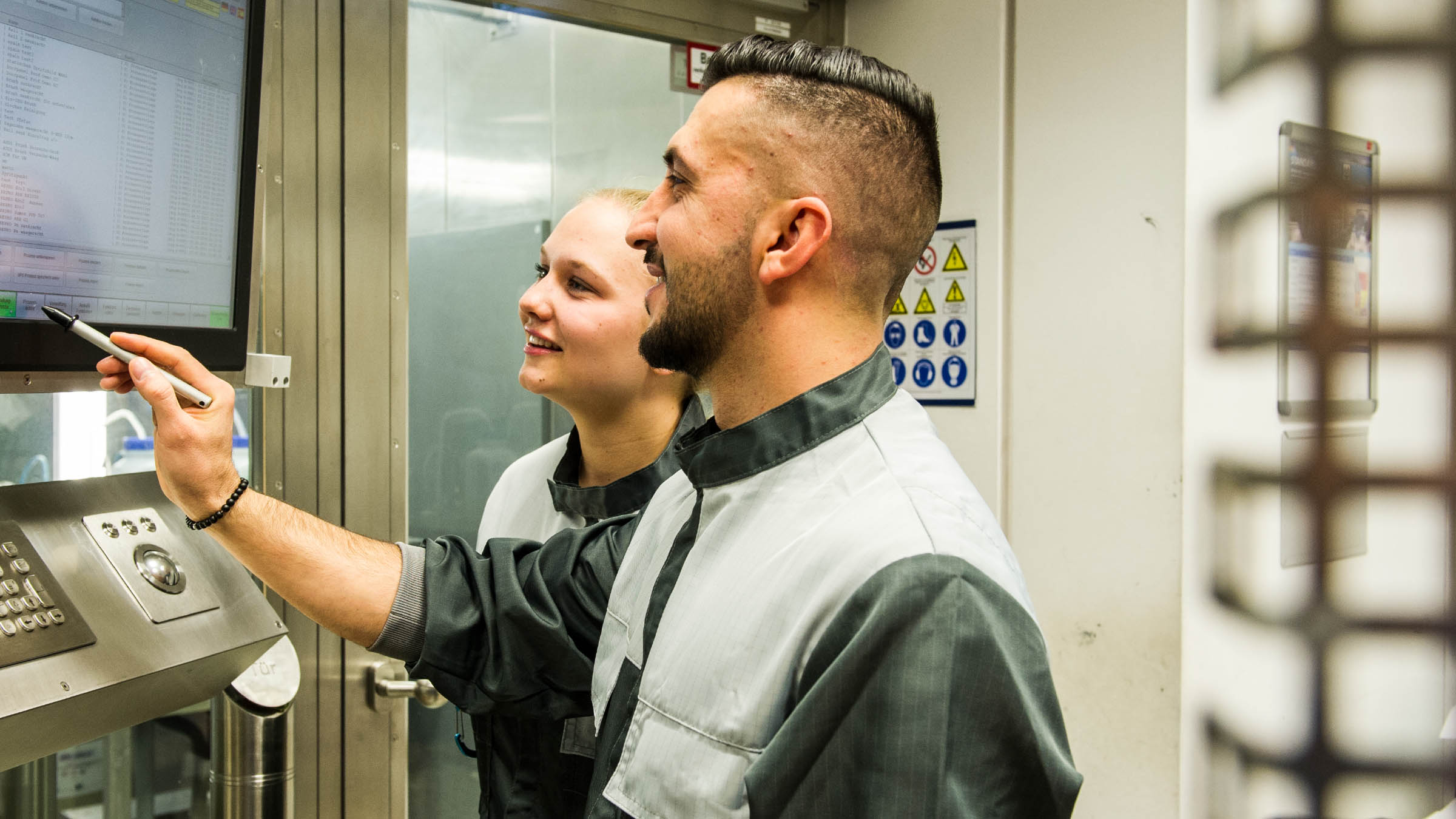 Mitarbeitende in Schutzkleidung bedienen gemeinsam ein digitales Steuerpult in der Produktion.