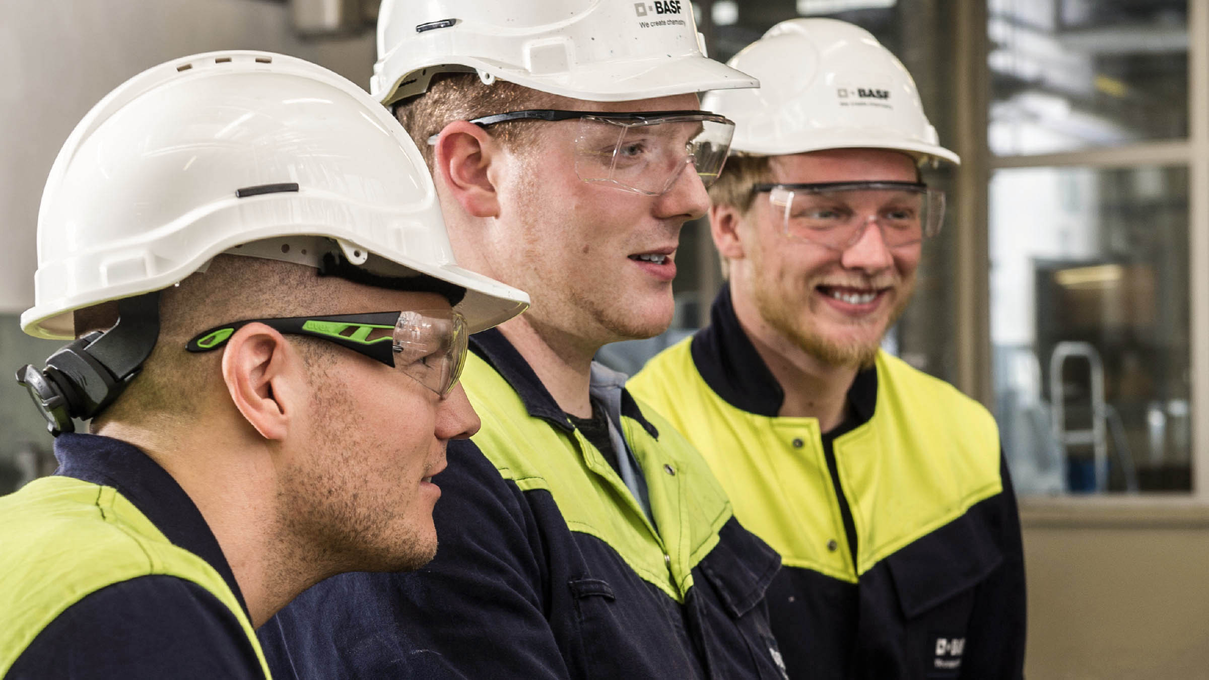 Mitarbeiter von BASF Coatings in Schutzausrüstung lächeln während eines Arbeitseinsatzes in der Produktion.