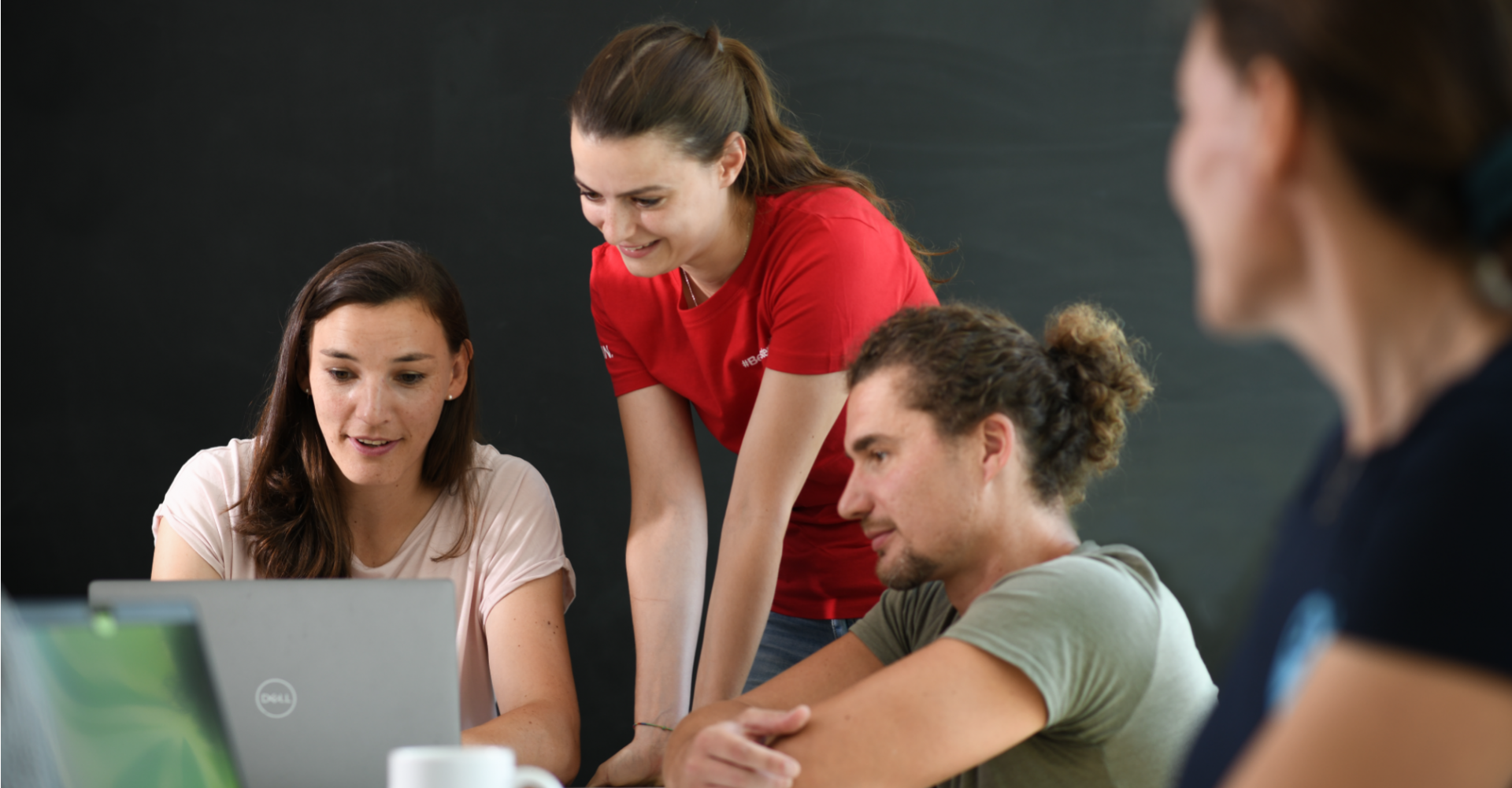 Vier Mitarbeitende von Garmin arbeiten gemeinsam an einem Laptop und sprechen miteinander in einem Meetingraum.