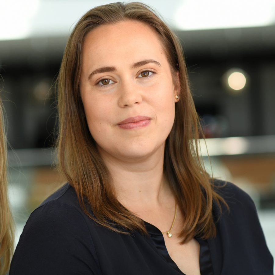 Porträtaufnahme einer jungen Frau in dunkler Bluse, die freundlich in die Kamera blickt.