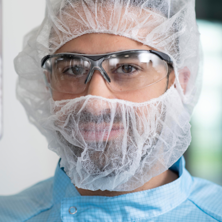 Mitarbeiterin im Reinraum bei Boehringer Ingelheim mit Schutzhaube, Schutzanzug und Handschuhen während der Arbeit an einer Anlage.