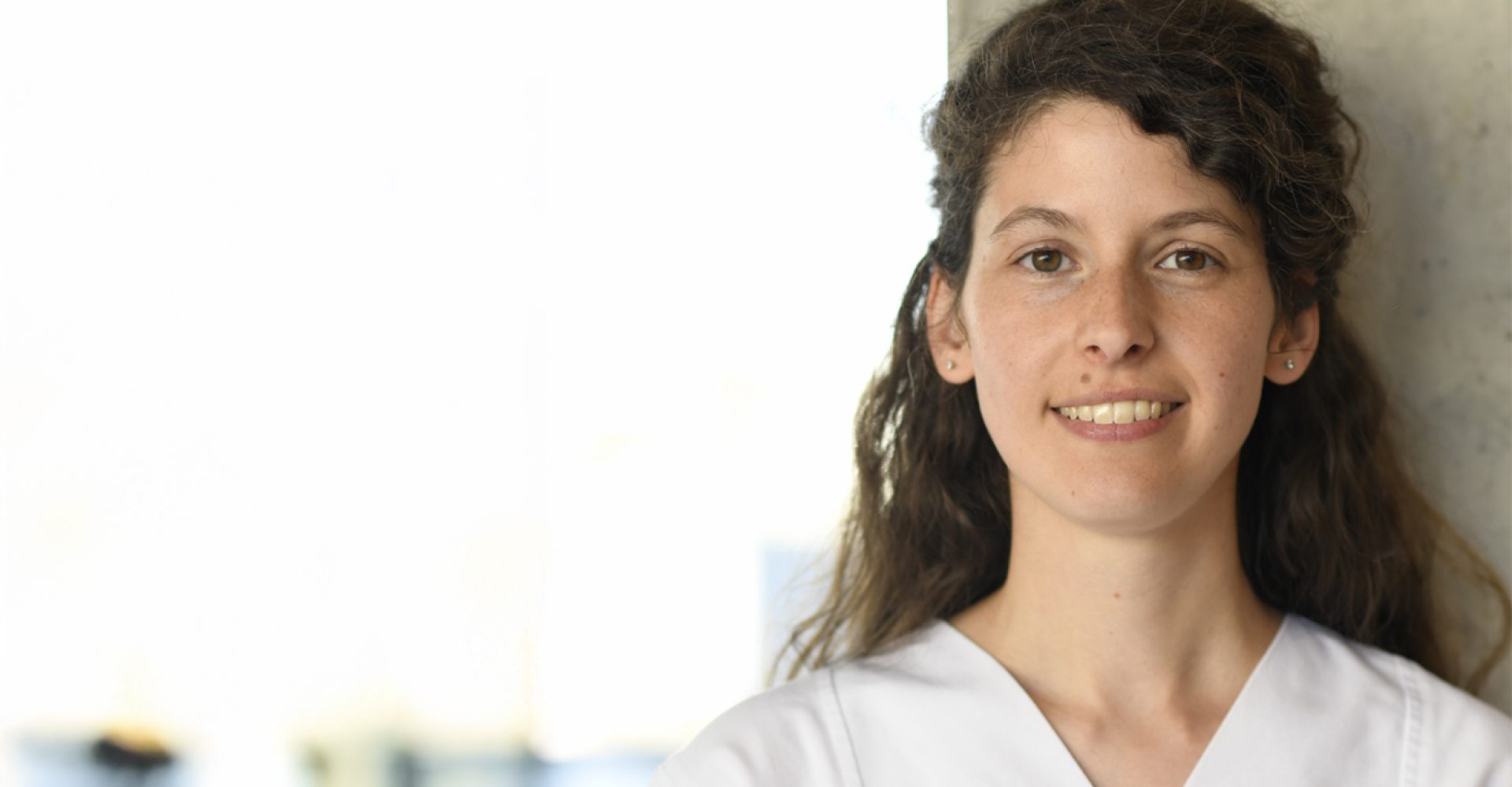 Pflegekraft der Uniklinik Würzburg lächelt in moderner Klinikumgebung.